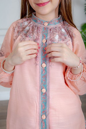 طقم تيور بناتي قطعتين لون خربزي بلوزة بياقة عالية و أزرار من الأمام ذو أكمام طويلة و تـنورة مزين بزخارف ملونة من الأطراف و الأكمام 