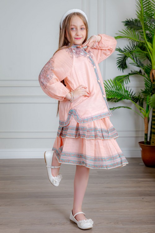 طقم تيور بناتي قطعتين لون خربزي بلوزة بياقة عالية و أزرار من الأمام ذو أكمام طويلة و تـنورة مزين بزخارف ملونة من الأطراف و الأكمام