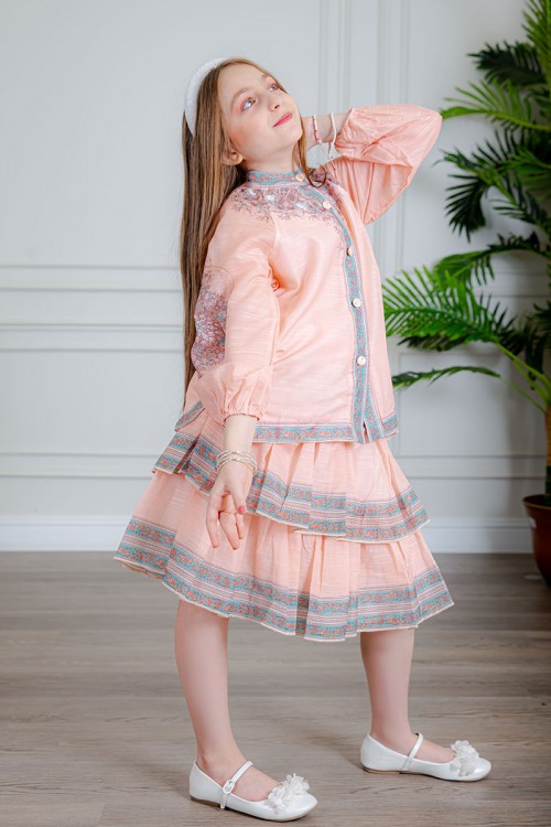 طقم تيور بناتي قطعتين لون خربزي بلوزة بياقة عالية و أزرار من الأمام ذو أكمام طويلة و تـنورة مزين بزخارف ملونة من الأطراف و الأكمام