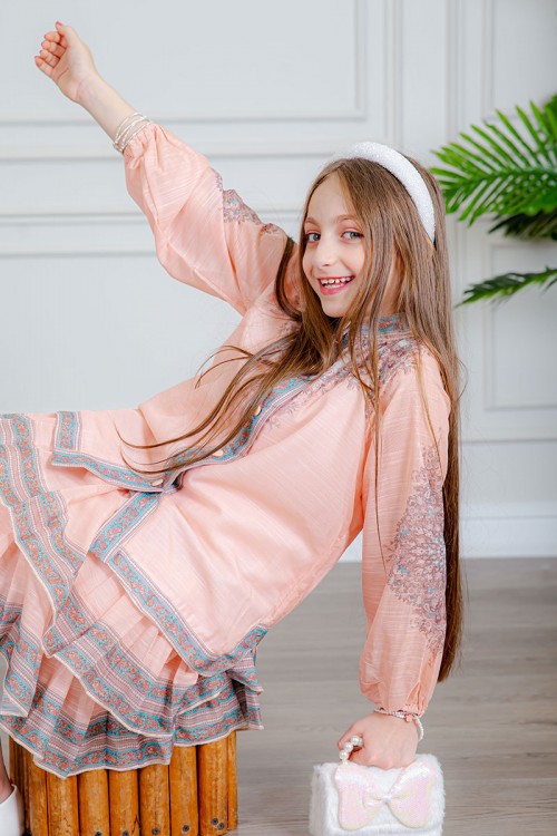 طقم تيور بناتي قطعتين لون خربزي بلوزة بياقة عالية و أزرار من الأمام ذو أكمام طويلة و تـنورة مزين بزخارف ملونة من الأطراف و الأكمام