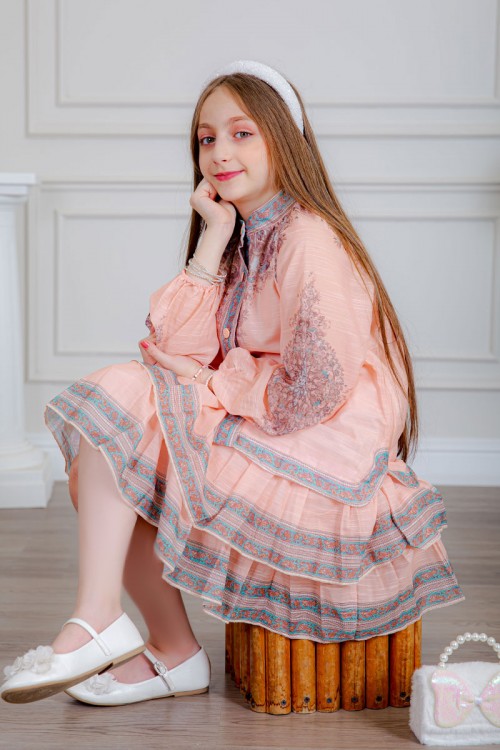 طقم تيور بناتي قطعتين لون خربزي بلوزة بياقة عالية و أزرار من الأمام ذو أكمام طويلة و تـنورة مزين بزخارف ملونة من الأطراف و الأكمام