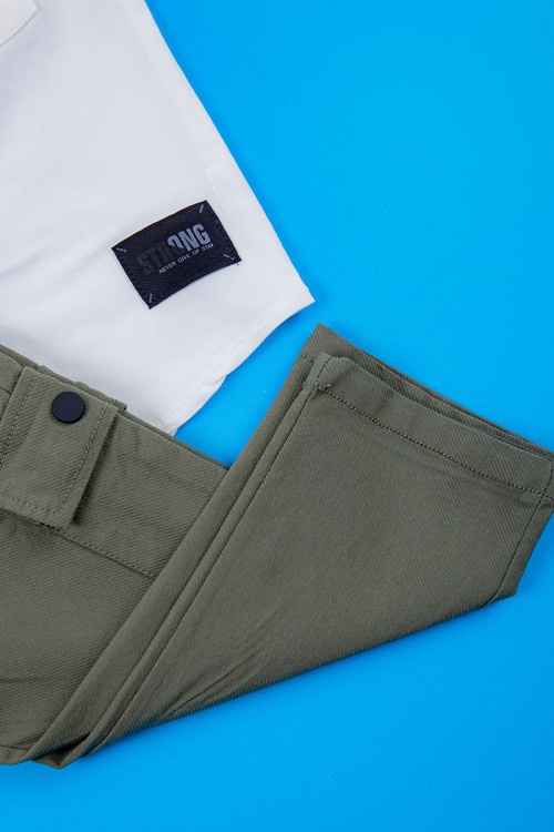 طقم ولادي قطعتين قميص أبيض بكتابات و جيب و أزرار من الأمام و بنطلون لون زيتي برباط في الخصر و جيوب من الجانبين