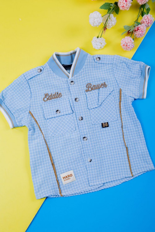 طقم ولادي قطعتين قميص سماوي مربعات بكتابات و جيبوب و أزرار من الأمام و بنطلون لون بيج غامق برباط في الخصر و جيوب من الجانبين