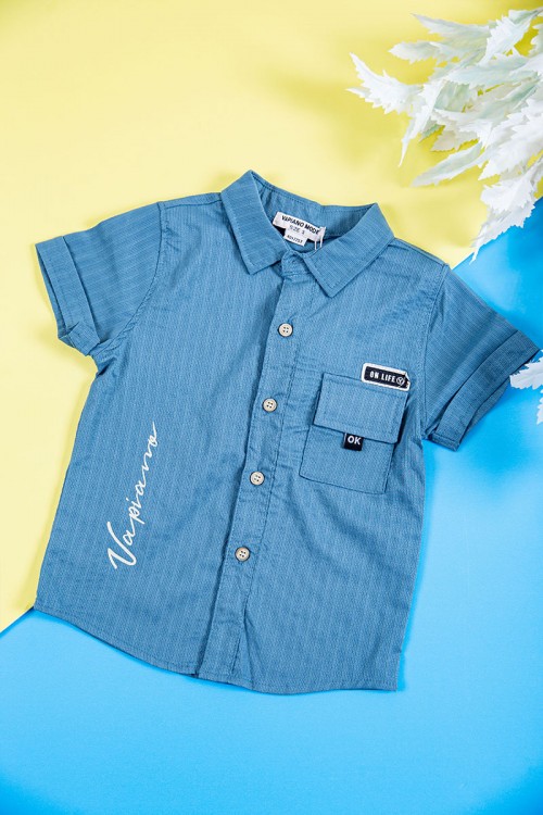 طقم ولادي قطعتين قميص لون سماوي بكتابات و طبعات و أزرار و جيب من الأمام و بنطلون طويل لون بيج فاتح برباط في الخصر و جيوب من الجانبين و الخلف