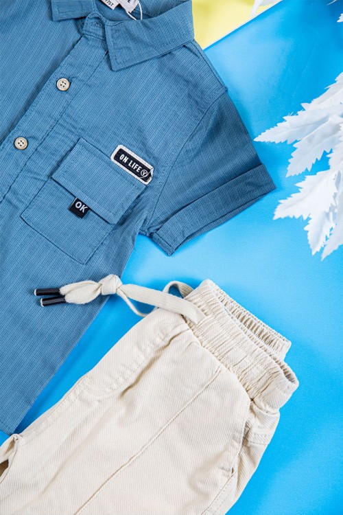 طقم ولادي قطعتين قميص لون سماوي بكتابات و طبعات و أزرار و جيب من الأمام و بنطلون طويل لون بيج فاتح برباط في الخصر و جيوب من الجانبين و الخلف