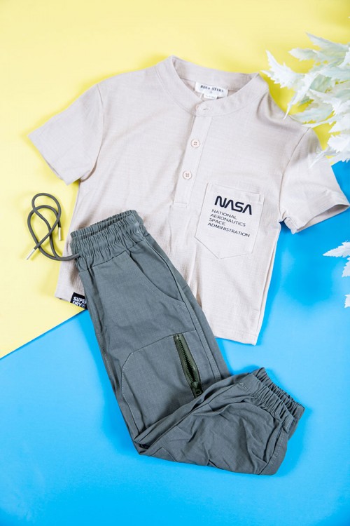 طقم ولادي قطعتين بلوزة لون بيج فاتح بكتابات و طبعات و أزرار و جيب من الأمام و بنطلون طويل لون رصاصي برباط في الخصر و جيوب و سحاب من الجانبين