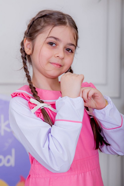 مريول بناتي مدرسي لون وردي مع قميص أبيض متصل و بأكتاف كرانيش و جيوب من الجانبين و رباط في الخصر