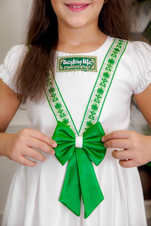 فستان بناتي لون أبيض مزين بتطريز اليوم الوطني ياقة دائرية بأكمام قصيرة و فيونكة من الأمام و رباط من الخلف