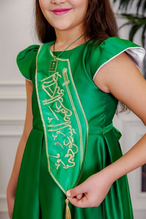 فستان بناتي لليوم الوطني لون أخضر مزين بوشاح من الأمام بتطريز عبارة المملكة العربية السعودية باللون الذهبي بأكمام قصيرة و رباط في الخلف مع تعليقة بشعار سيفين و نخلة 