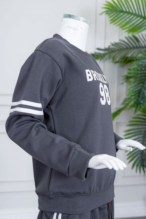 طقم بناتي شتوي قطعتين لون رصاصي بلوزة بياقة دائرية مزين بكتابات و خطوط باللون الأبيض بأكمام طويلة مع بنطلون طويل برباط في الخصر و جيوب من الجانبين