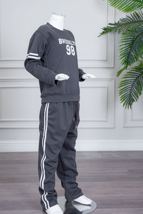 طقم بناتي شتوي قطعتين لون رصاصي بلوزة بياقة دائرية مزين بكتابات و خطوط باللون الأبيض بأكمام طويلة مع بنطلون طويل برباط في الخصر و جيوب من الجانبين