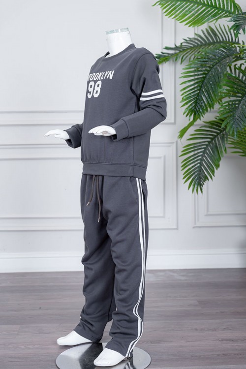 طقم بناتي شتوي قطعتين لون رصاصي بلوزة بياقة دائرية مزين بكتابات و خطوط باللون الأبيض بأكمام طويلة مع بنطلون طويل برباط في الخصر و جيوب من الجانبين