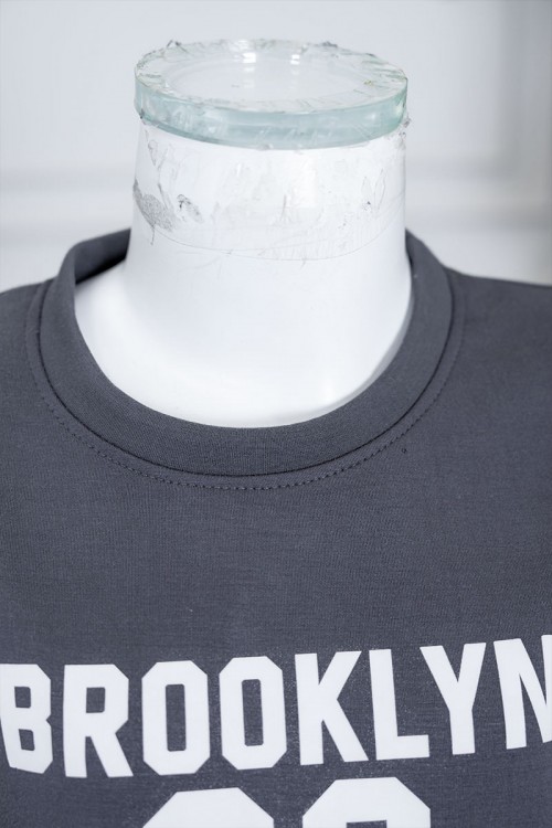 طقم بناتي شتوي قطعتين لون رصاصي بلوزة بياقة دائرية مزين بكتابات و خطوط باللون الأبيض بأكمام طويلة مع بنطلون طويل برباط في الخصر و جيوب من الجانبين