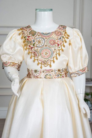 فستان بناتي طويل لون بيج فاتح مزين بتطريز ملون من الياقة و أطراف الأكمام و بحزام في الخصر 