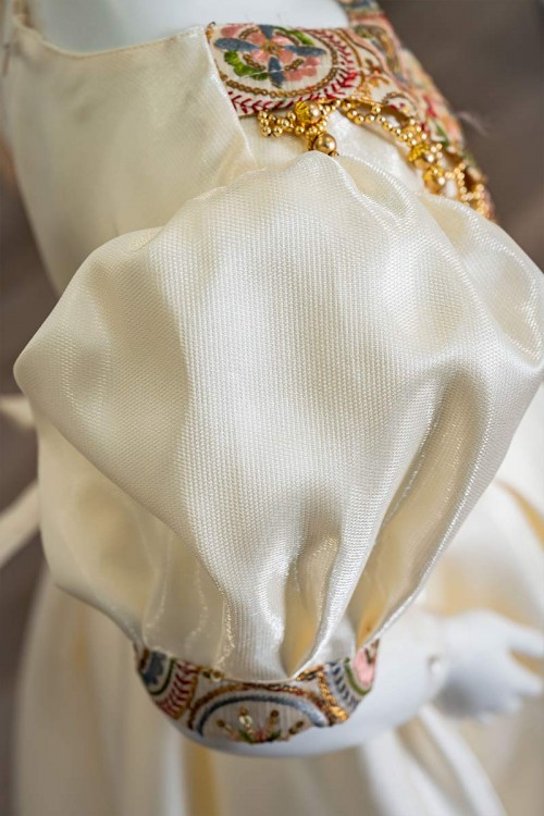 فستان بناتي طويل لون بيج فاتح مزين بتطريز ملون من الياقة و أطراف الأكمام و بحزام في الخصر