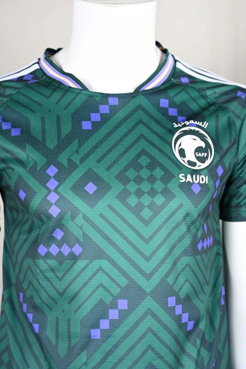 تيشيرت المنتخب السعودي لون أخضر داكن مع الشعار مزين بنمط هندسي و بزخارف ومنسوجات تراثية سعودية ياقة دائرية بلونين الأخضر و البنفسجي و بأكمام قصيرة