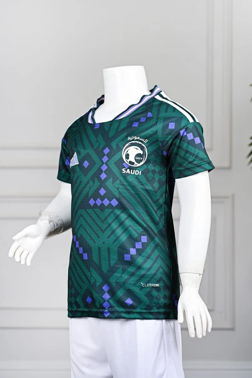 تيشيرت المنتخب السعودي شبابي لون أخضر داكن مع الشعار مزين بنمط هندسي و بزخارف ومنسوجات تراثية سعودية ياقة دائرية بلونين الأخضر و البنفسجي و بأكمام قصيرة