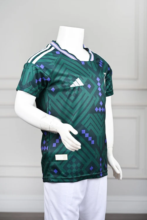 تيشيرت المنتخب السعودي شبابي لون أخضر داكن مع الشعار مزين بنمط هندسي و بزخارف ومنسوجات تراثية سعودية ياقة دائرية بلونين الأخضر و البنفسجي و بأكمام قصيرة
