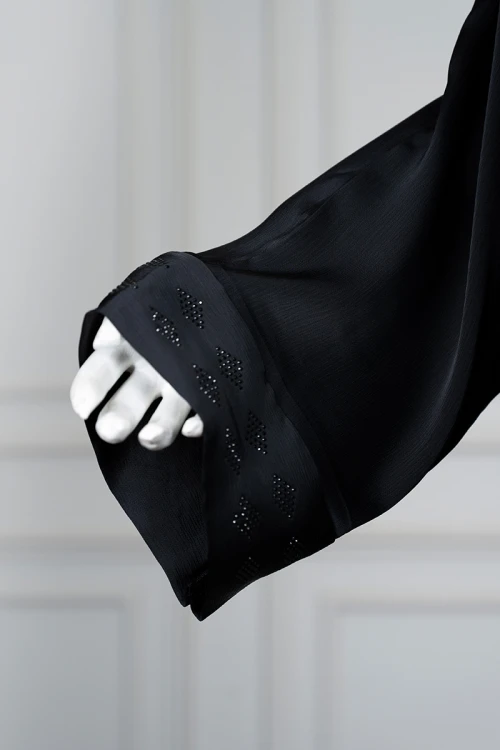 عباءة نسائية لون أسود مزينة بفصوص باللون الأسود ممتد على طول الياقة و المنتصف و أطراف الأكمام بأزرار طقطق من الأمام