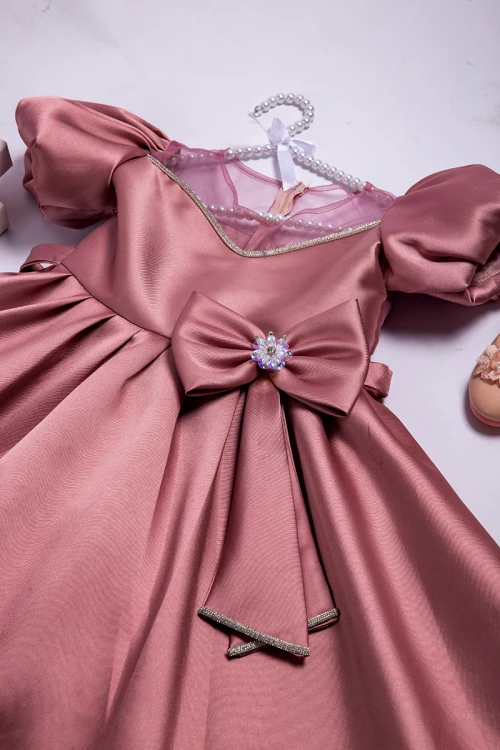 فستان بناتي أنيق لون وردي أكمام منفوشة وصدر قماش تل شفاف بتطريز كريستال فضي وفيونكة كبيرة على الخصر