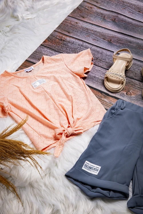 طقم بناتي أنيق قطعتين بلوزة لون برتقالي فاتح بشعار و رباط من الأمام و شورت مطاطي باللون الرمادي