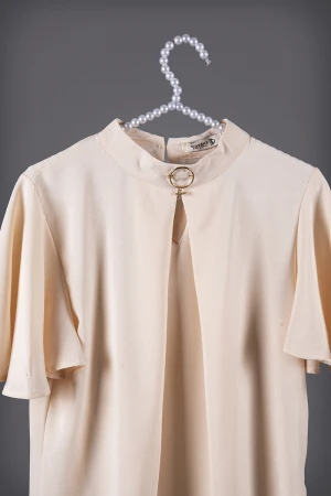 بلوزة نسائي أنيقة لون بيج أكمام قصيرة واسعة و ياقة عالية مزين بإكسسوار ذهبي من الأمام  وفتحة من الأمام  