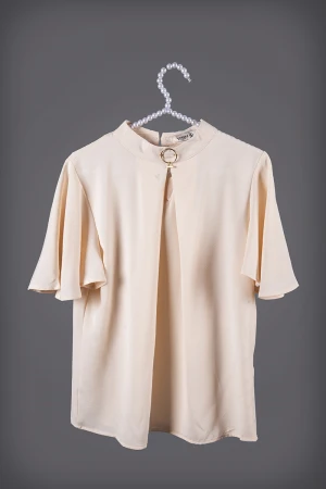 بلوزة نسائي أنيقة لون بيج أكمام قصيرة واسعة و ياقة عالية مزين بإكسسوار ذهبي من الأمام  وفتحة من الأمام  