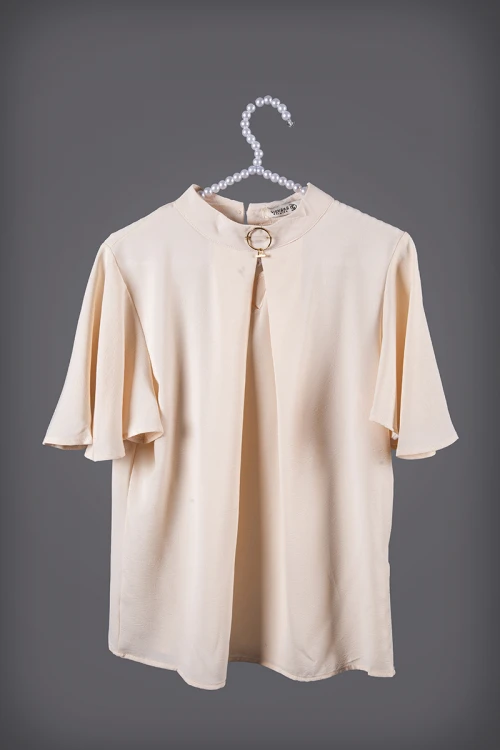 بلوزة نسائي أنيقة لون بيج أكمام قصيرة واسعة و ياقة عالية مزين بإكسسوار ذهبي من الأمام  وفتحة من الأمام