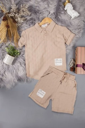 طقم ولادي قطعتين لون بيج أكمام قصيرة بياقة وأزرار قفل وطبعات من الامام وشورت بجيوب و رباط من الخصر