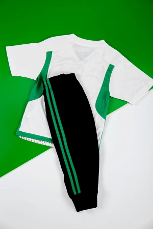 طقم ولادي رياضي قطعتين تيشيرت لون أبيض مزين باللون الأخضر و الوردي بأكمام قصيرة و بنطلون طويل لون أسود مخطط باللون الأخضر من الجانبين بزم من الخصر و الأسفل