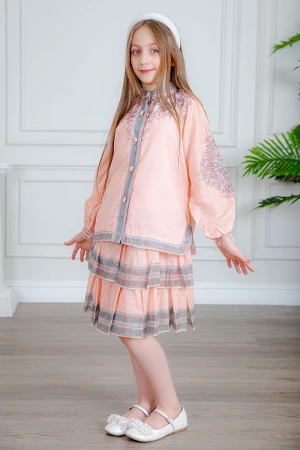 طقم تيور بناتي قطعتين لون خربزي بلوزة بياقة عالية و أزرار من الأمام ذو أكمام طويلة و تـنورة مزين بزخارف ملونة من الأطراف و الأكمام 