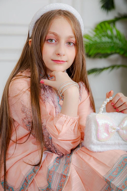 طقم تيور بناتي قطعتين لون خربزي بلوزة بياقة عالية و أزرار من الأمام ذو أكمام طويلة و تـنورة مزين بزخارف ملونة من الأطراف و الأكمام