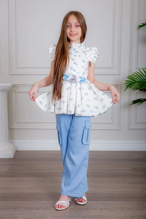 بدلة بناتي قطعتين بلوزة لون أبيض بياقة عالية بدون أكمام مزينة بورود سماوية و أزرار من الأمام و حزام في الخصر مع بنطلون طويل لون سماوي بجيوب من الجانبين