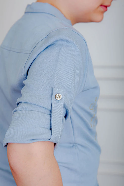 بدلة ولادي قطعتين قميص لون سماوي  بأزرار و جيب و كتابات من الأمام و بنطلون لون بيج بجيوب من الجانبين و الخلف و برباط في الخصر