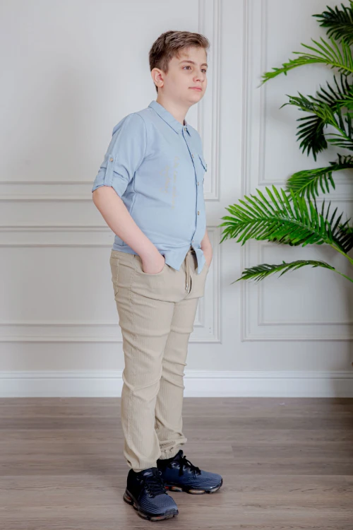 بدلة ولادي قطعتين قميص لون سماوي  بأزرار و جيب و كتابات من الأمام و بنطلون لون بيج بجيوب من الجانبين و الخلف و برباط في الخصر