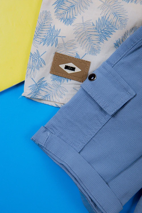 طقم ولادي قطعتين قميص أبيض مشجر باللون السماوي ياقة مطوية و أزرار من الأمام و شورت لون سماوي برباط في الخصر و جيوب من الجانبين