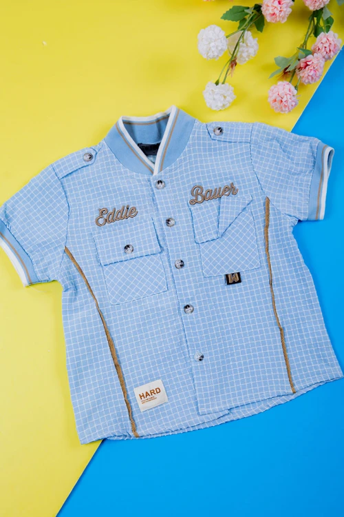 طقم ولادي قطعتين قميص سماوي مربعات بكتابات و جيبوب و أزرار من الأمام و بنطلون لون بيج غامق برباط في الخصر و جيوب من الجانبين