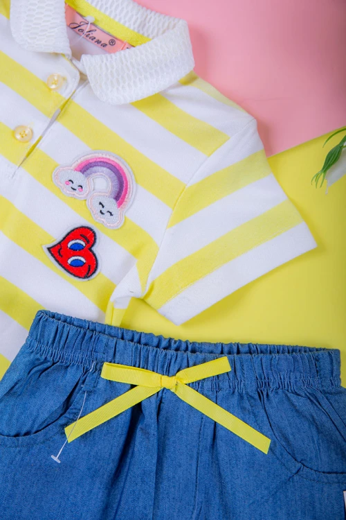 طقم بناتي قطعتين بلوزة مخططة بأزرار من الأمام مزينة بطبعات مع شورت جينز بخصر مطاطي و جيوب من الجانبين مزين بفيونكة من الأمام