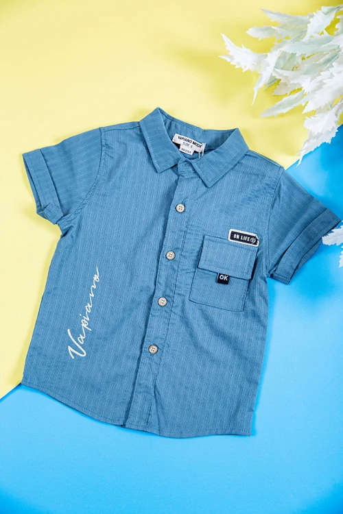 طقم ولادي قطعتين قميص لون سماوي بكتابات و طبعات و أزرار و جيب من الأمام و بنطلون طويل لون بيج فاتح برباط في الخصر و جيوب من الجانبين و الخلف