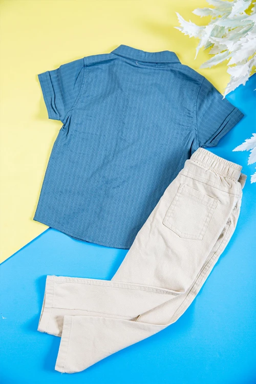 طقم ولادي قطعتين قميص لون سماوي بكتابات و طبعات و أزرار و جيب من الأمام و بنطلون طويل لون بيج فاتح برباط في الخصر و جيوب من الجانبين و الخلف