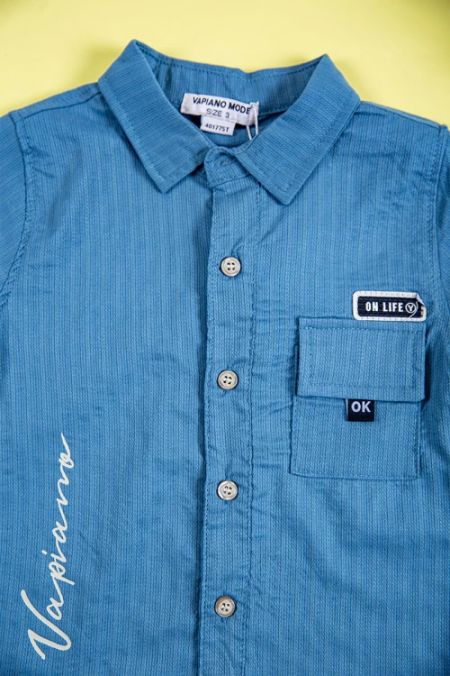 طقم ولادي قطعتين قميص لون سماوي بكتابات و طبعات و أزرار و جيب من الأمام و بنطلون طويل لون بيج فاتح برباط في الخصر و جيوب من الجانبين و الخلف