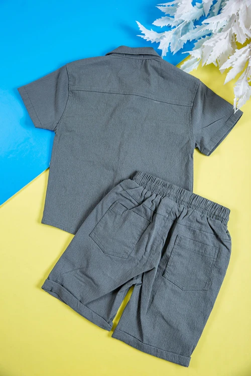 طقم ولادي قطعتين لون رصاصي قميص بكتابات و طبعات وجيوب وازرار من الأمام و شورت برباط في الخصر و جيوب من الجانبين و الخلف