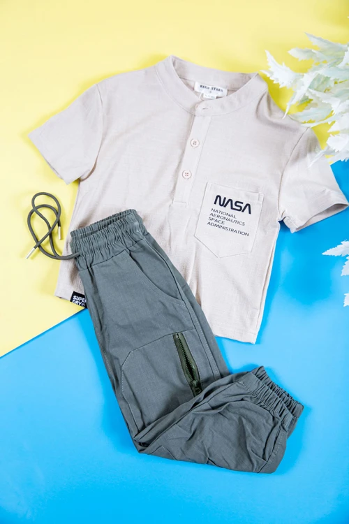 طقم ولادي قطعتين بلوزة لون بيج فاتح بكتابات و طبعات و أزرار و جيب من الأمام و بنطلون طويل لون رصاصي برباط في الخصر و جيوب و سحاب من الجانبين