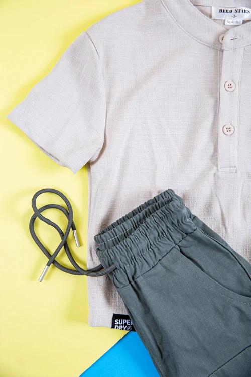 طقم ولادي قطعتين بلوزة لون بيج فاتح بكتابات و طبعات و أزرار و جيب من الأمام و بنطلون طويل لون رصاصي برباط في الخصر و جيوب و سحاب من الجانبين