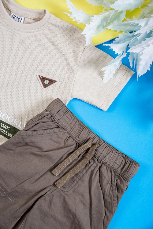 طقم ولادي قطعتين تيشيرت لون بيج فاتح بكتابات و طبعات من الأمام و بنطلون طويل لون بني بجيوب من الجانبين