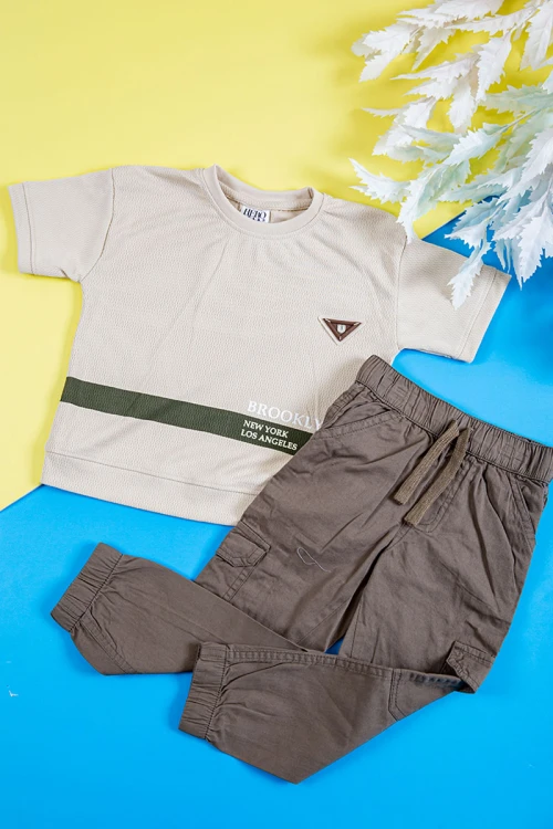 طقم ولادي قطعتين تيشيرت لون بيج فاتح بكتابات و طبعات من الأمام و بنطلون طويل لون بني بجيوب من الجانبين