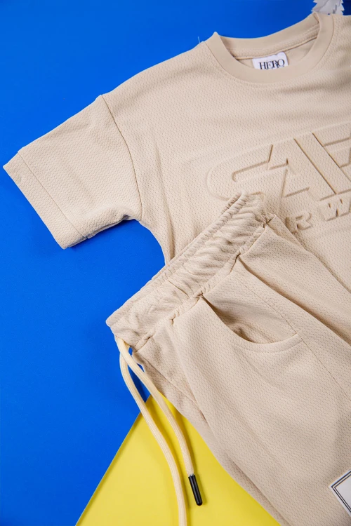 طقم ولادي قطعتين لون بيج تيشيرت بكتابات و طبعات من الأمام و شورت برباط في الخصر و جيوب من الجانبين