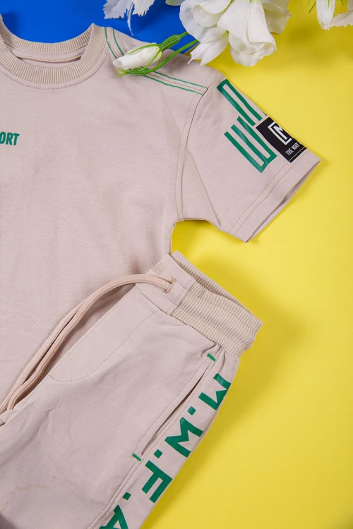 طقم ولادي قطعتين لون بيج تيشيرت بكتابات باللون الأخضر و طبعات و بنطلون طويل برباط في الخصر و جيوب من الجانبين وزم في الأسفل