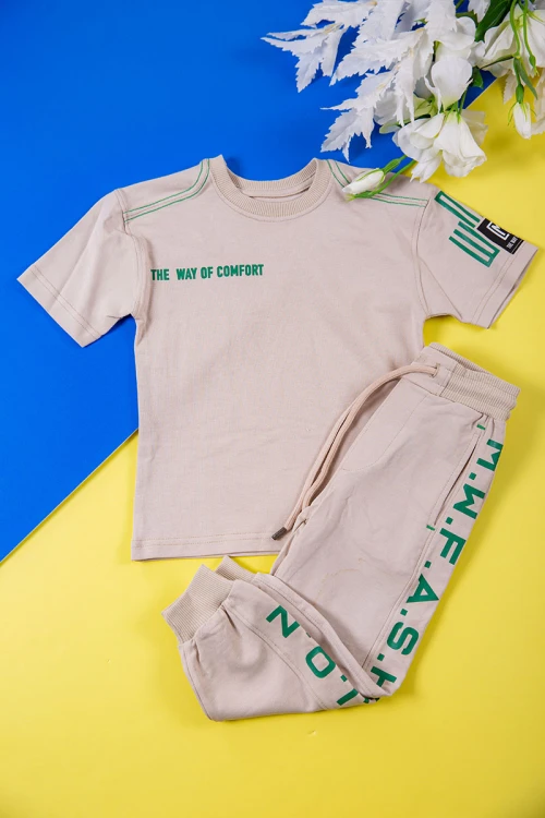 طقم ولادي قطعتين لون بيج تيشيرت بكتابات باللون الأخضر و طبعات و بنطلون طويل برباط في الخصر و جيوب من الجانبين وزم في الأسفل