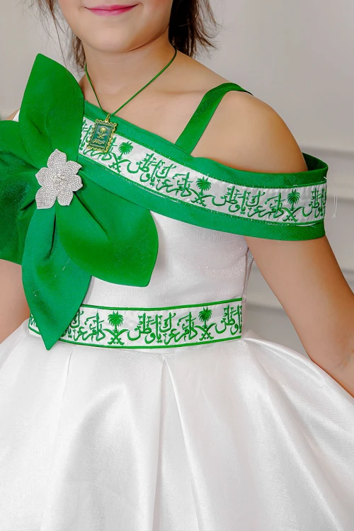 فستان بناتي لليوم الوطني لون أبيض مزين بوردة خضراء و كتابات مطرزة